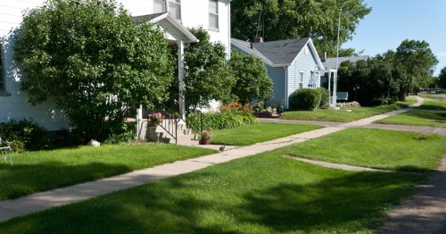 A peaceful neighborhood scene with well-maintained lawns, sidewalks, and charming houses surrounded by greenery.