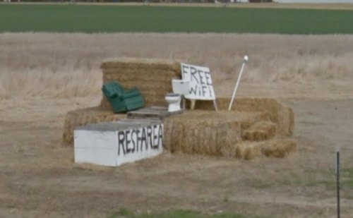 A makeshift seating area made of hay bales, featuring a toilet and signs for "Free Wi-Fi" and "Rest Area."