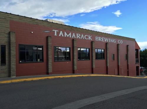 Exterior of Tamarack Brewing Co. building with large windows and a red facade against a blue sky.