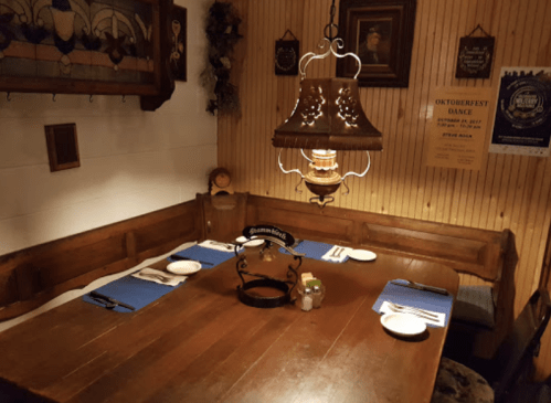 Cozy restaurant interior with wooden seating, a vintage lamp, and a table set for dining. Oktoberfest poster on the wall.