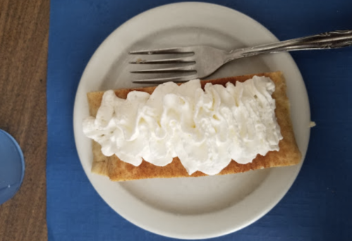 A plate with a dessert topped with whipped cream, served with a fork on a blue table.
