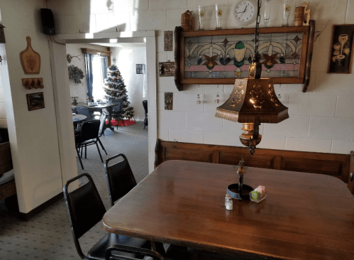 Cozy dining area with a wooden table, vintage lamp, and a view of a decorated Christmas tree in the next room.