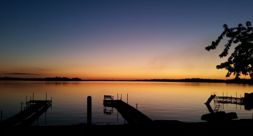 A serene lake at sunset, with silhouettes of docks and trees against a colorful sky.