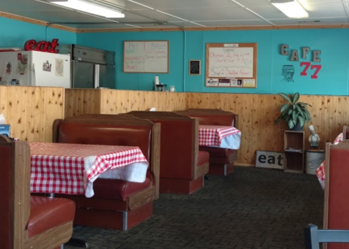 Cozy diner interior with red checkered tablecloths, wooden booths, and a bright blue wall featuring a menu board.