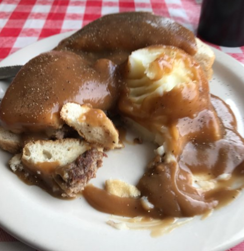 A plate with two pieces of bread topped with gravy and a serving of mashed potatoes smothered in brown gravy.