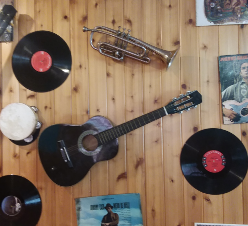 A wooden wall displays a guitar, trumpet, vinyl records, and music posters, creating a vintage music vibe.