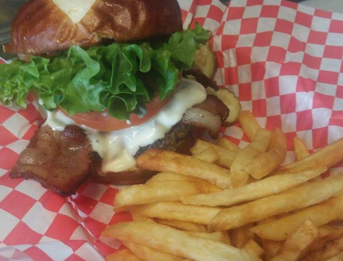 A juicy burger with lettuce, tomato, and bacon on a pretzel bun, served with a side of golden French fries.