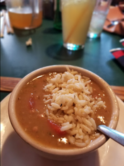 A bowl of soup with rice on top, served on a plate, with drinks in the background.