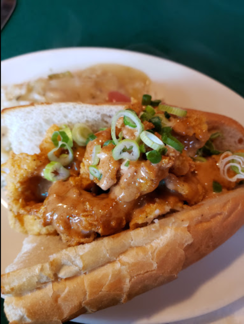 A close-up of a sandwich filled with fried shrimp, topped with green onions and a savory sauce, served on a soft bun.