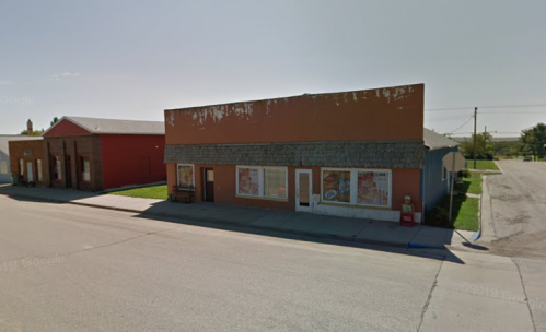 A small, weathered storefront with colorful signage, located on a quiet street in a rural area.