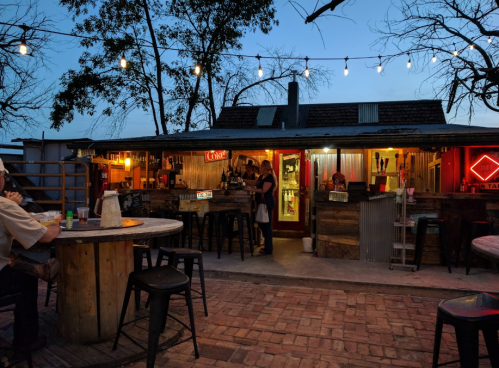A cozy outdoor bar at dusk, with string lights, wooden tables, and a welcoming atmosphere.