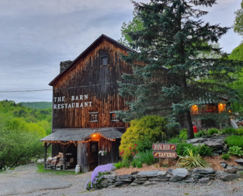 A rustic barn restaurant surrounded by greenery, with string lights and a sign for a tavern.