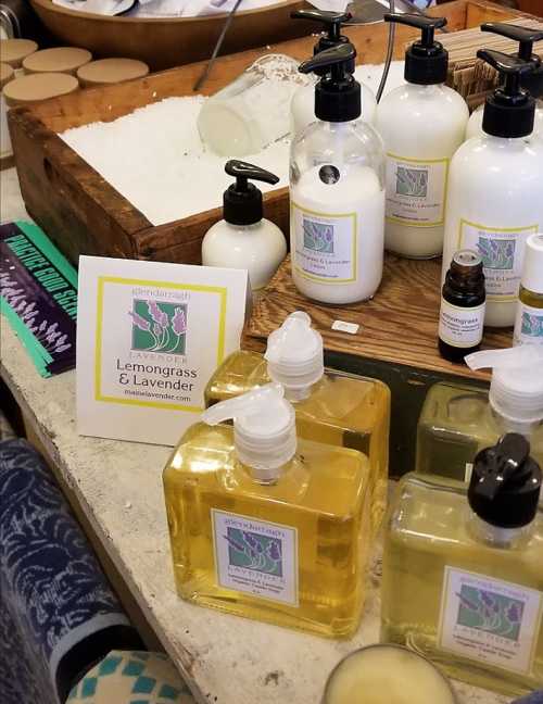 Bottles of lemongrass and lavender products displayed on a table with a sign and wooden containers.