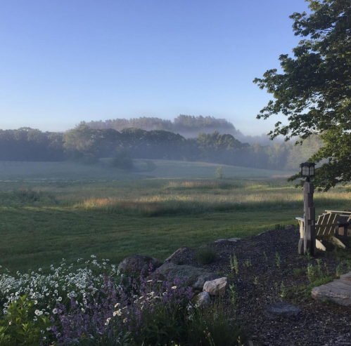 A serene landscape at dawn, featuring misty hills, lush greenery, and a peaceful seating area.