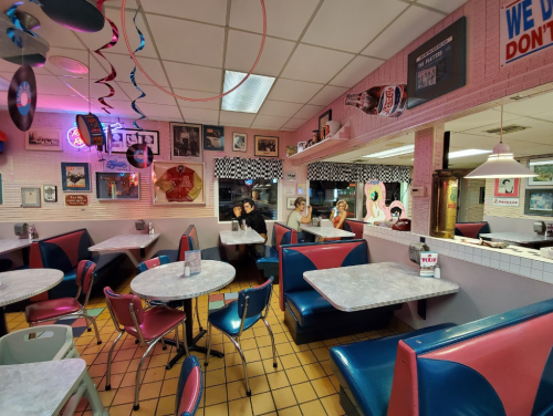 A retro diner interior with pink and blue decor, featuring empty booths and vintage memorabilia on the walls.