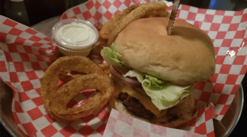 A cheeseburger with lettuce, onion, and a side of onion rings on a red and white checkered plate.