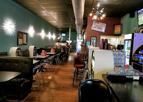 A retro diner interior with booths, a bar, and a jukebox, featuring teal walls and wooden floors.