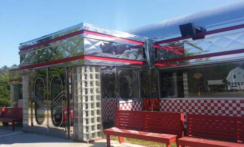 A shiny, retro diner with mirrored exterior, red accents, and glass block windows, surrounded by red benches.