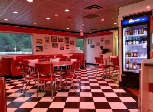 Retro diner interior with red booths, checkered floor, and a Pepsi fridge, creating a nostalgic atmosphere.