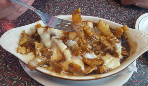 A dish of poutine with fries, cheese curds, and gravy, served in a white dish with a fork.