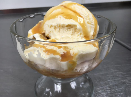 A glass bowl filled with creamy vanilla ice cream drizzled with caramel sauce.