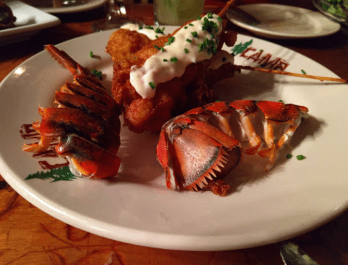 A plate featuring grilled lobster claws, fried seafood, and a dipping sauce, garnished with chives.