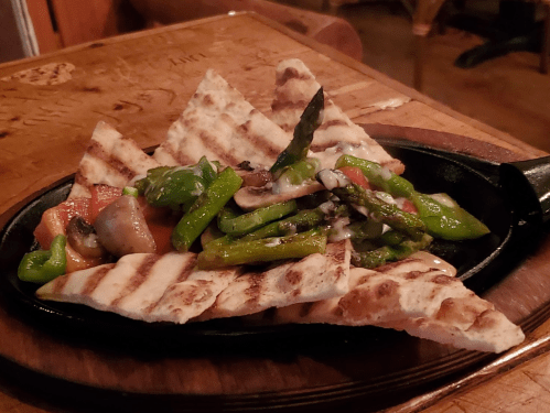 Grilled vegetables and flatbread served on a sizzling platter, garnished with herbs.