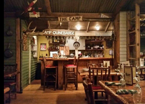 Cozy rustic restaurant interior with wooden furniture, a bar, and decor featuring signs and antlers.