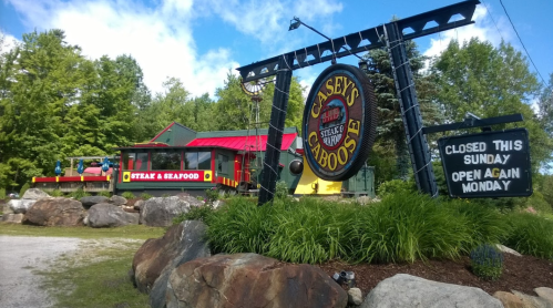 Sign for Casey's Caboose, a steak and seafood restaurant, with a colorful exterior and rocky landscaping.