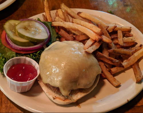 A cheeseburger with melted cheese, lettuce, tomato, pickles, and a side of fries and ketchup on a plate.