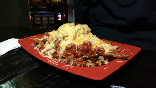A red plate piled high with loaded fries topped with cheese, chili, and a generous portion of melted cheese.