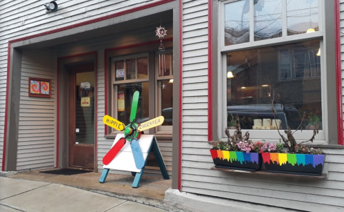Colorful storefront with a propeller sign reading "Hippie Chickpea" and flower boxes under the windows.