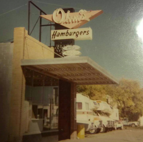 Vintage photo of a hamburger restaurant with a retro sign, featuring a drive-thru and parked RVs nearby.