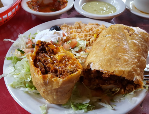 A plate featuring a crispy burrito, rice, lettuce, diced tomatoes, sour cream, and two types of salsa.