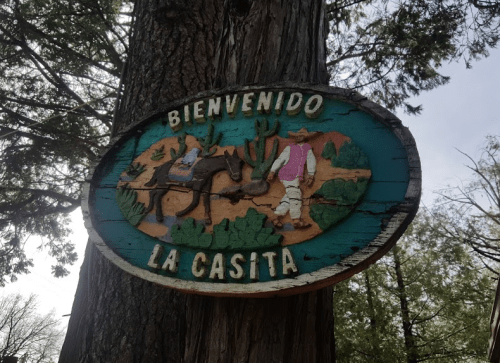 Colorful wooden sign reading "Bienvenido La Casita," depicting a scene with a horse and two figures in a natural setting.