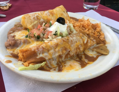 A plate of enchiladas topped with cheese, sour cream, and olives, served with rice and refried beans on the side.