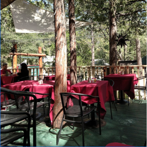 Outdoor dining area with red tablecloths, surrounded by trees and a relaxed atmosphere.