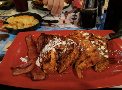 A red plate with grilled chicken, bacon, and powdered sugar, alongside a side of cheesy potatoes.