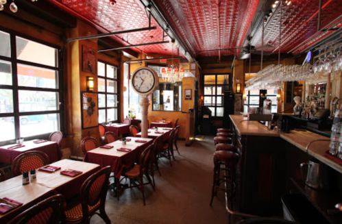 Cozy restaurant interior with red ceiling, wooden bar, tables set for dining, and large clock on the wall.