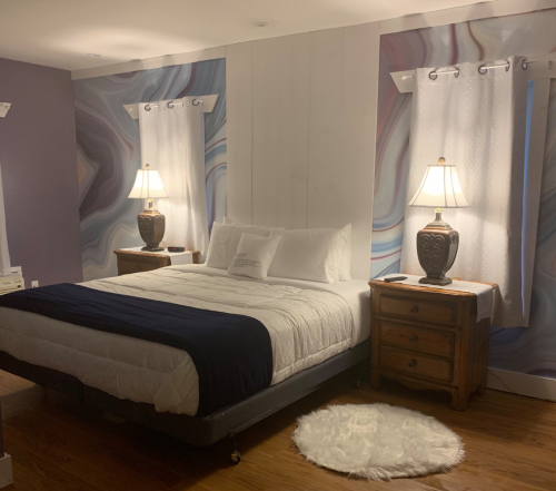 Cozy bedroom with a large bed, two lamps, wooden nightstands, and colorful abstract wall design.