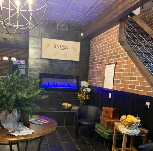 Cozy entryway with a round table, plants, blue electric fireplace, and decorative brick walls. Warm, inviting atmosphere.