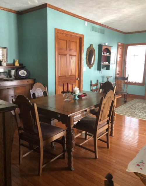 A cozy dining area with a wooden table, chairs, and teal walls, featuring vintage decor and warm wooden accents.