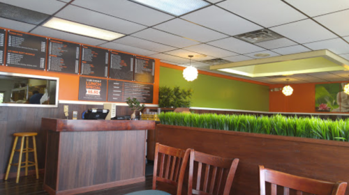 Interior of a restaurant featuring a menu board, wooden seating, and green decor with plants.