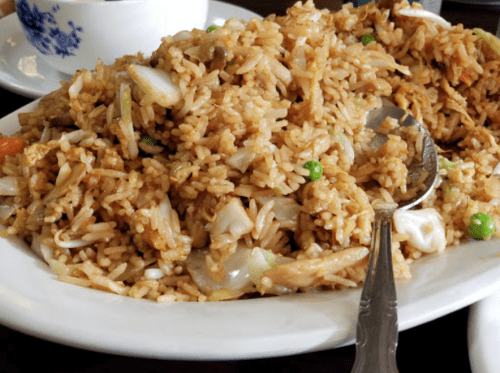 A close-up of a plate of fried rice with vegetables and pieces of chicken, served with a spoon.