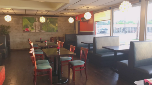 Interior of a restaurant featuring wooden tables, red chairs, and soft lighting, with a Buddha mural on the wall.
