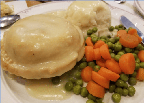 A plate of chicken pot pie with gravy, mashed potatoes, and a side of peas and carrots.