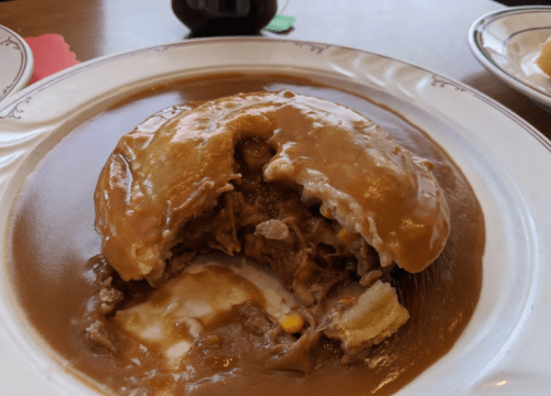 A plate with a large, round dish filled with meat and gravy, partially eaten, revealing its contents.