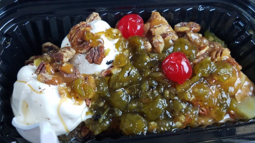 A dessert featuring two scoops of ice cream topped with nuts, cherries, and a green fruit sauce in a black container.