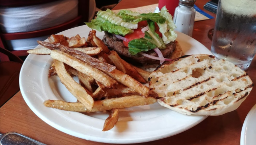 A plate with a grilled burger topped with lettuce, tomato, and onion, served with crispy fries and a toasted bun.