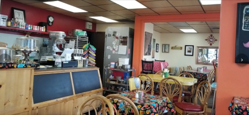 Cozy café interior with colorful tablecloths, wooden furniture, and a counter displaying baked goods.